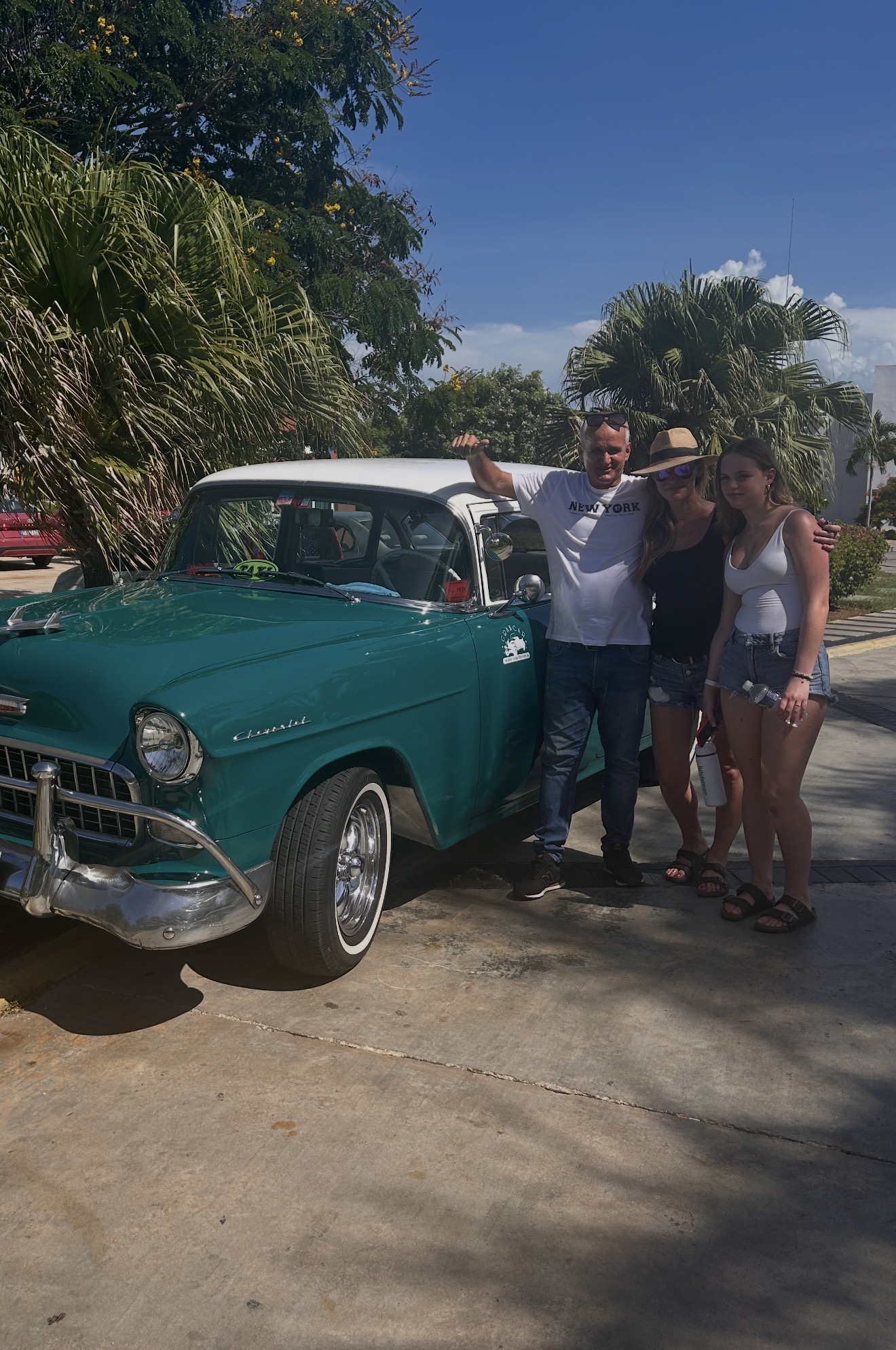 Family posing with their driver and his vintage teal Chevrolet in Cuba